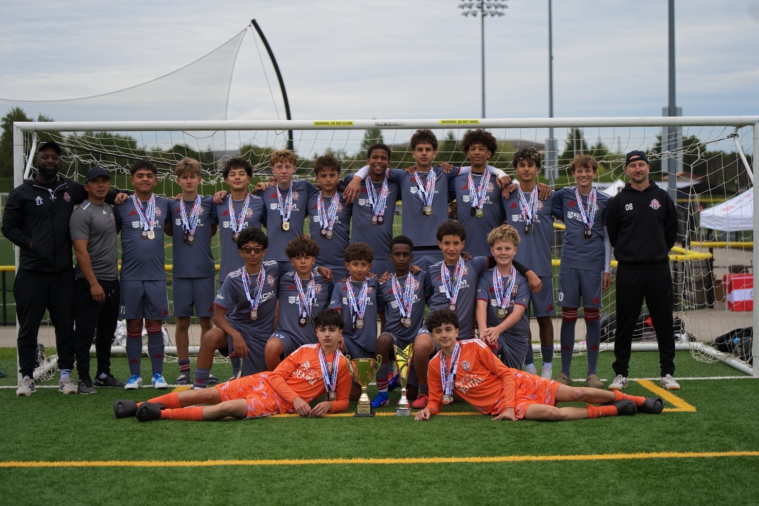 The team in grey championship kits posing with the trophy and coaching staff.