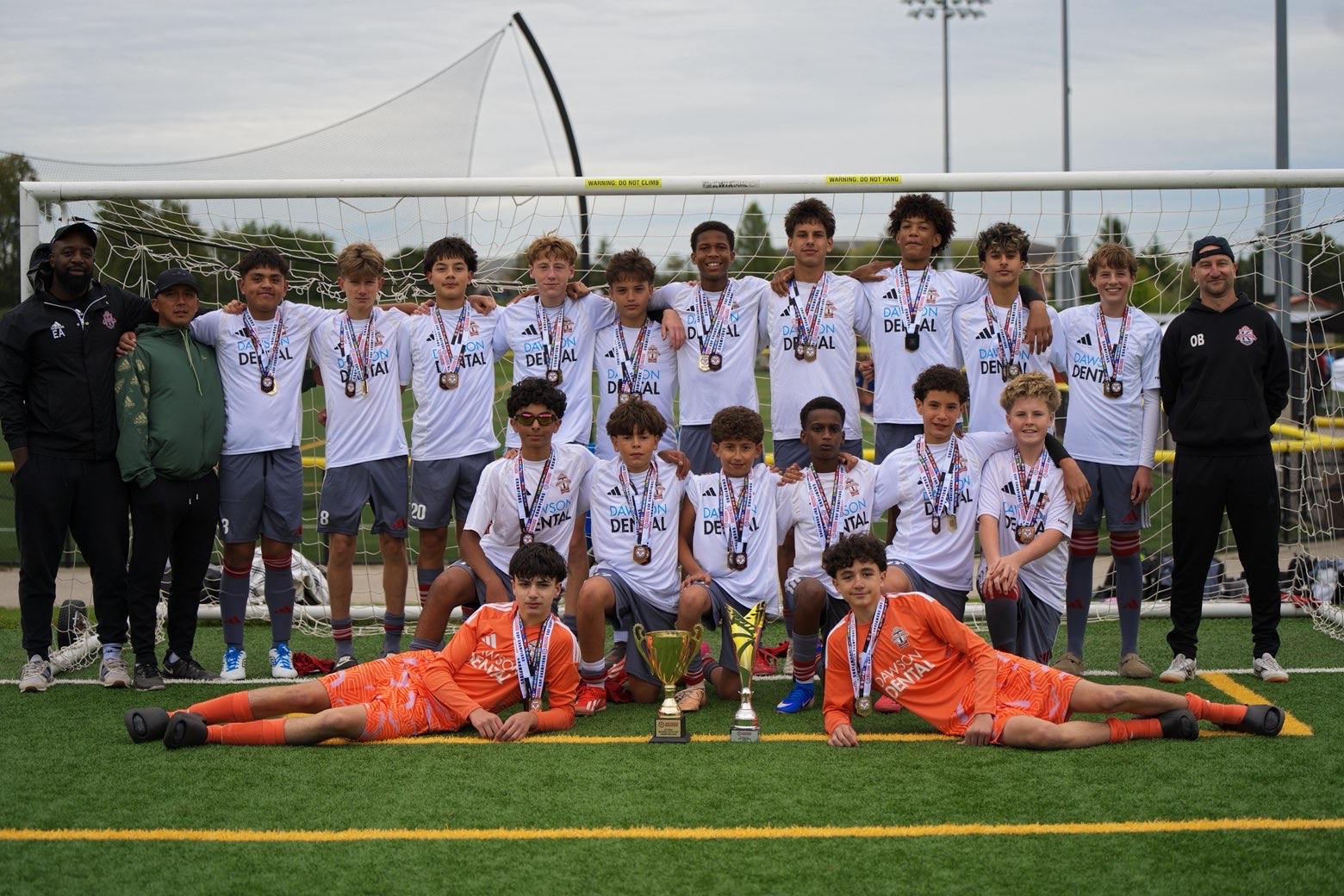 The team in white championship kits sponsored by Dawson Dental, posing with the trophy and coaching staff.